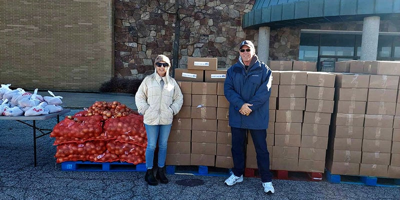 Community volunteers stand beside donated food supplies during a food distribution event serving Michigan City residents.